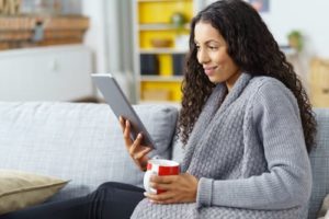 Woman in a gray sweater holding a red and white coffee mug reading a Real Estate Market Report on a tablet