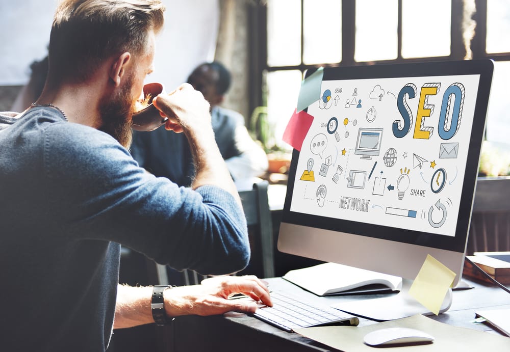 Man sits at computer drinking coffee looking at an SEO strategy