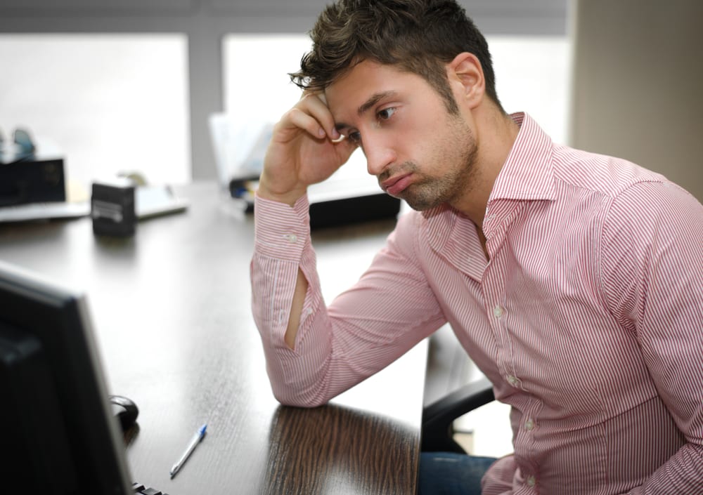 Young man in red shirt sits looking disappointed at his computer potentially looking at a website drop in traffic