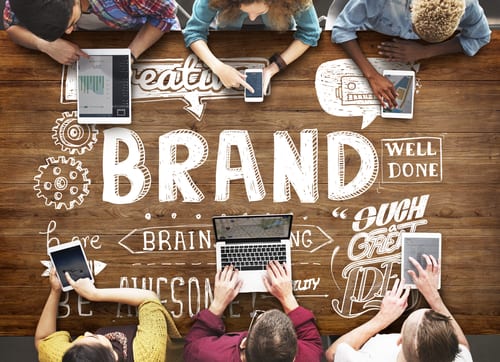 People are sitting around a table with computers, phones, tablets and the word BRAND is in the middle