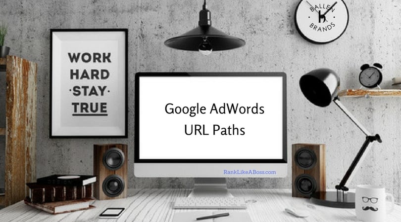 Google Adwords URL paths is spelled out on a computer screen on a desk with black lamp, sign that says work hard play, pen, mouse, phone