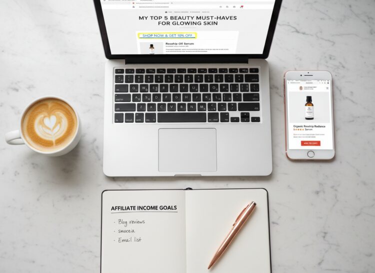 Laptop with a blog post and phone showing a product page on a marble desk — affiliate marketing examples