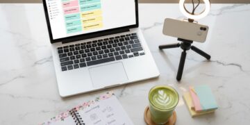 Laptop, phone on a tripod, and a content planning notebook on a marble desk — how to become a content creator